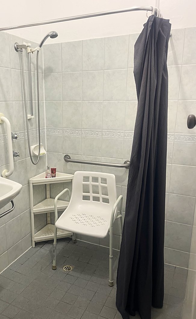 An accessible bathroom with grab rails, a hand-held shower and a shower chair