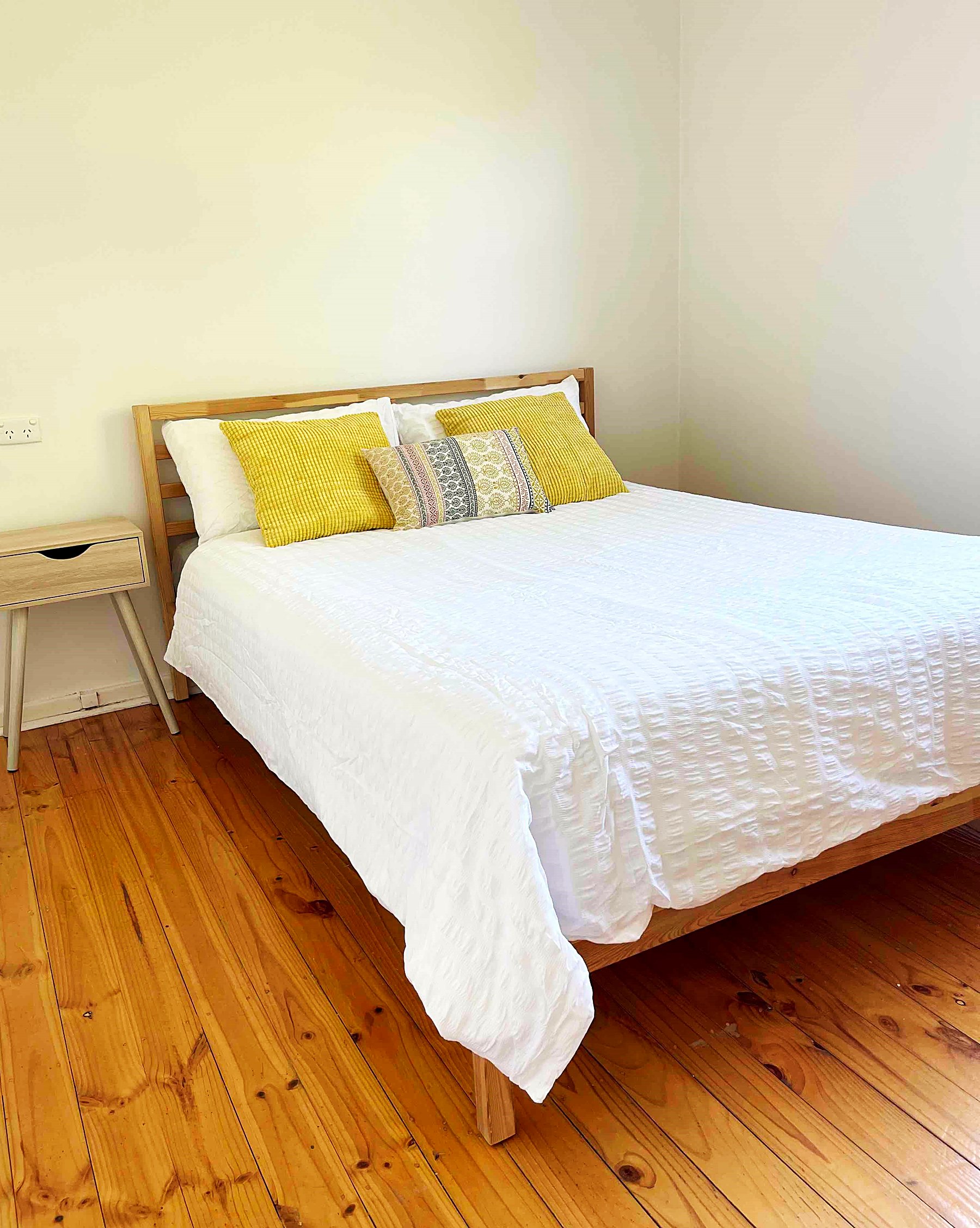 A furnished bedroom with a double bed, bedside table and polished timber floorboards